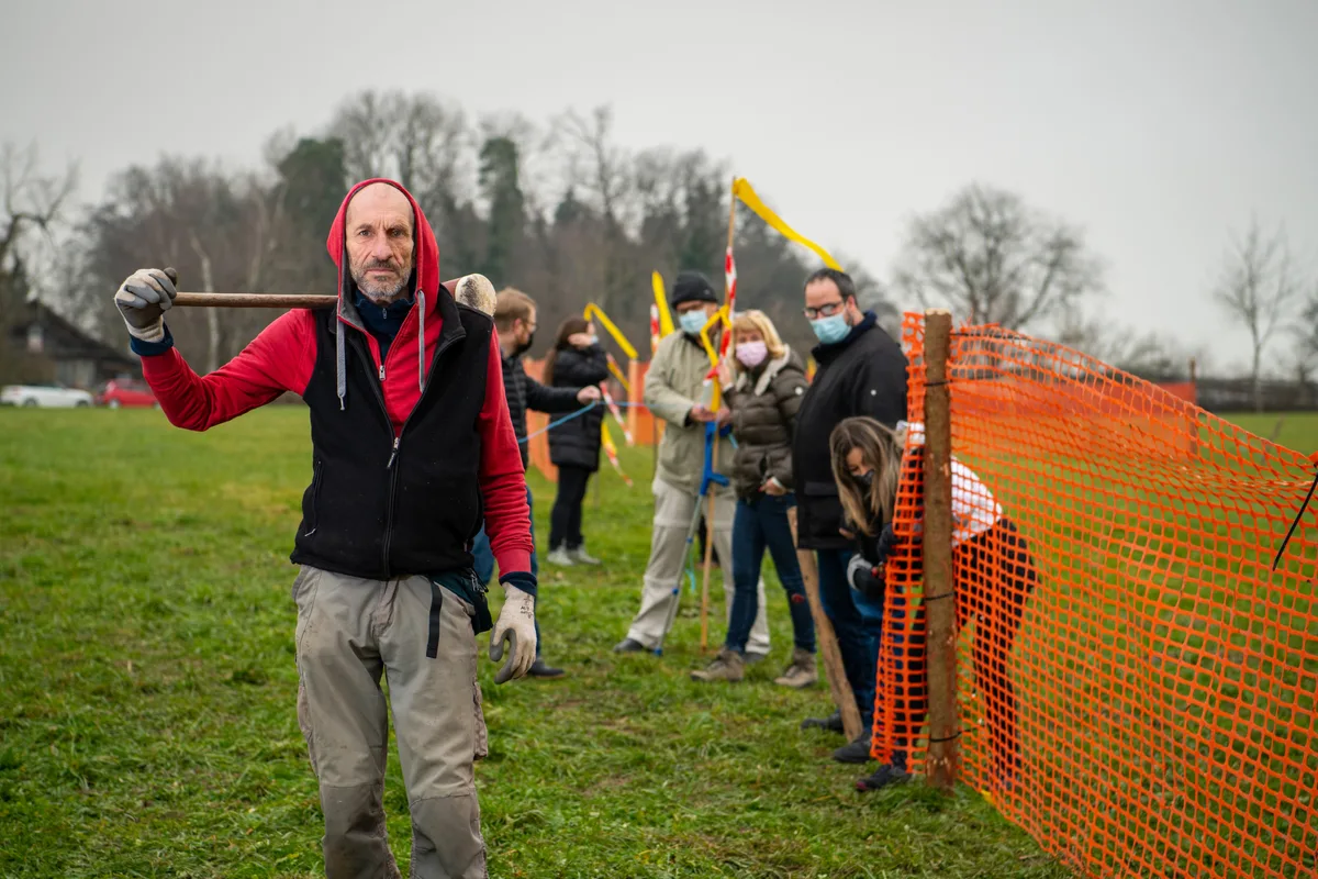 Die IG Pro Brach Fuchsbühl umzäunte die betroffene Fläche in Bubikon in einer Protestaktion. (Archiv) Mehrere Menschen stellen einen roten Zaun um eine Wiese.